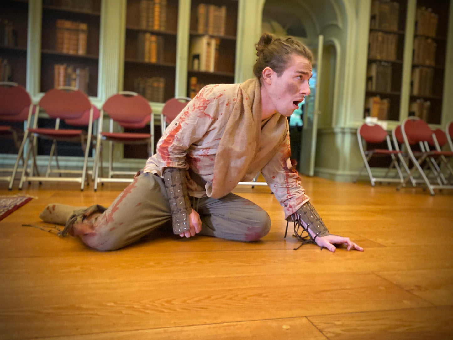 Cast of Valkyrie Productions' Pay No Heed in historical costume kneeling on a wooden floor with bookshelves in the background