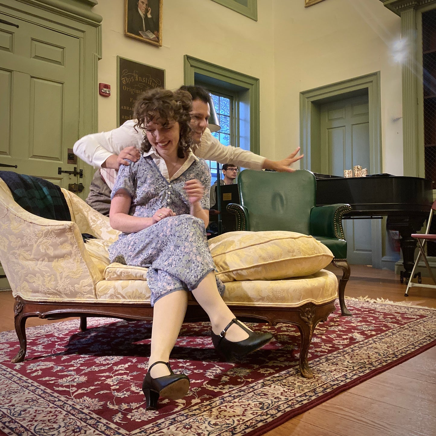 Cast of Valkyrie Productions' Pay No Heed in a room on a yellow setee with a piano and decorative furniture.